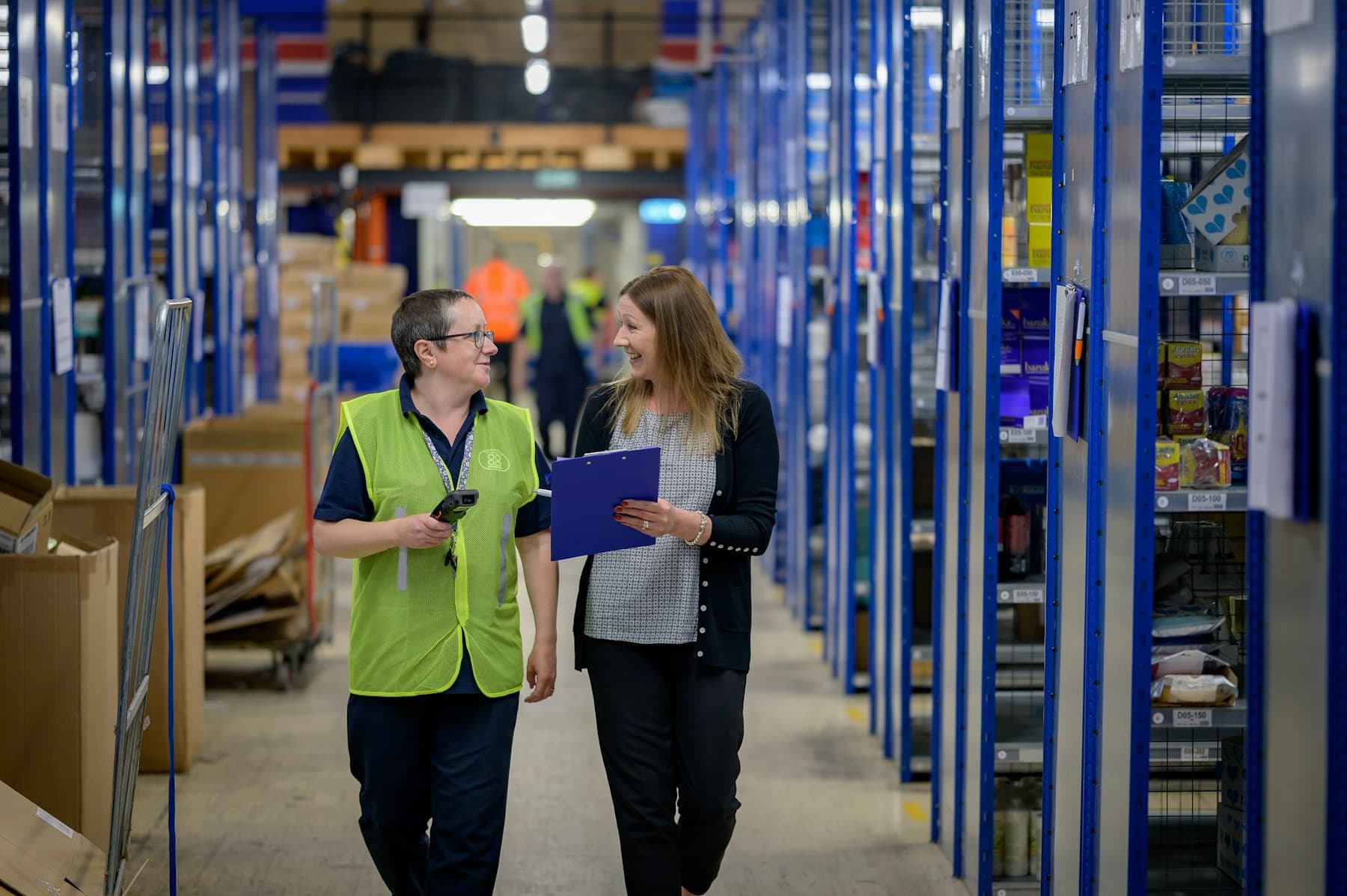 Two people walking through a warehouse aisle with tall shelving